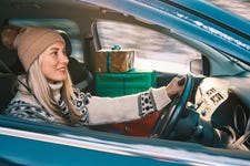 Woman Giving Gifts. Female is holding presents and delivering them on her car to Home. Holidays concept. Driving car in Christmas Eve. People In A Snow-Covered Forest. Sunny Cold Winter Day.