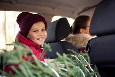 Smiling little boy sitting in a car near the just buyed christmas tree, in anticipation of happy holidays. Mother driving home with her son from xmas market.