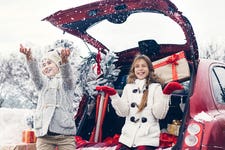 Holiday preparations. Pre teen children enjoy many Christmas presents in car trunk. Cold winter, snow weather.