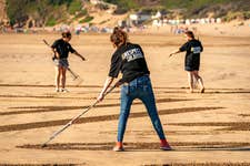 EDITORIAL USE ONLY People rake sand to create a 75-metre piece of sand art depicting a military Chinook helicopter on Saunton Sands beach in Devon as part of the Defence Infrastructure Organisation (DIO) ëRespect the Rangeí campaign, warning holidaymakers and locals to check military firing and training times when accessing Ministry of Defence (MOD) sites this summer. Issue date: Thursday August 4, 2022. PA Photo. The safety initiative aims to warn visitors about the risks they face when entering shared land used by the MOD for training, including live firing, unexploded ordnance and fast-moving military vehicles. Sites that pose significant risk to locals and tourists include Lulworth, Holbeach, Donna Nook, Barry Buddon, Lydd & Hythe, Salisbury Plain and Aldershot.