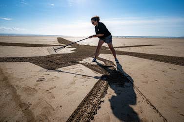 EDITORIAL USE ONLY People rake sand to create a 75-metre piece of sand art depicting a military Chinook helicopter on Saunton Sands beach in Devon as part of the Defence Infrastructure Organisation (DIO) ëRespect the Rangeí campaign, warning holidaymakers and locals to check military firing and training times when accessing Ministry of Defence (MOD) sites this summer. Issue date: Thursday August 4, 2022. PA Photo. The safety initiative aims to warn visitors about the risks they face when entering shared land used by the MOD for training, including live firing, unexploded ordnance and fast-moving military vehicles. Sites that pose significant risk to locals and tourists include Lulworth, Holbeach, Donna Nook, Barry Buddon, Lydd & Hythe, Salisbury Plain and Aldershot.